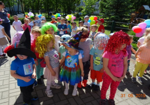 Dzieci min. w perukach i kapeluszach na tarsie przystrojonym balonami.